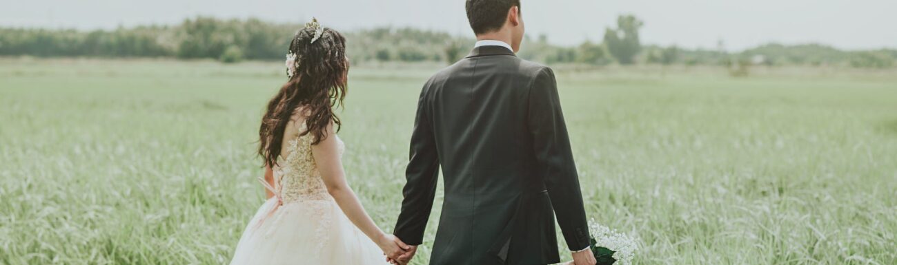 Woman in White Wedding Dress Holding Hand to Man in Black Suit